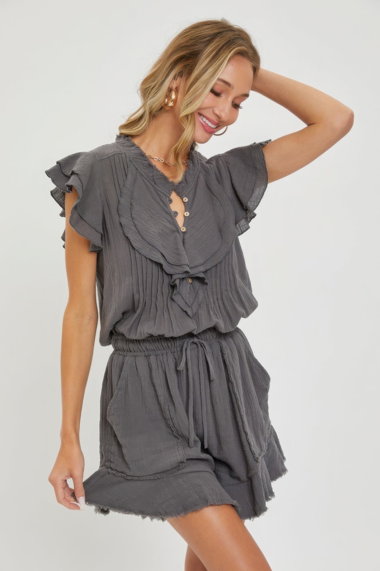 Woman wearing a grey ruffle romper with button-up front and drawstring waist for a stylish and comfortable spring/summer look.