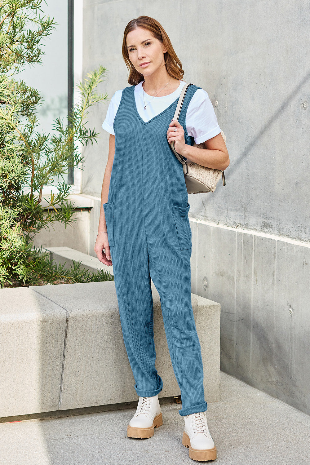 Woman wearing a sleeveless straight jumpsuit with pockets and a white shirt, standing outdoors.