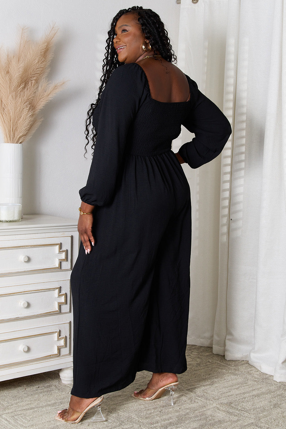 Woman wearing black square neck jumpsuit with long sleeves and pockets, showcasing chic style and flattering fit.