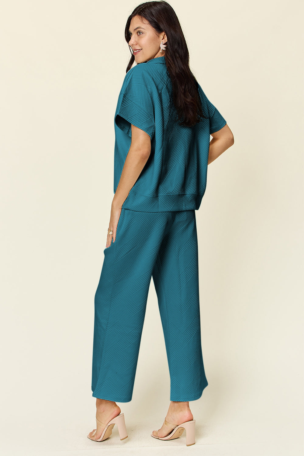 Woman wearing teal two-piece set with half zip top and wide-leg pants, pocketed design, made from slightly stretchy polyester-spandex blend.