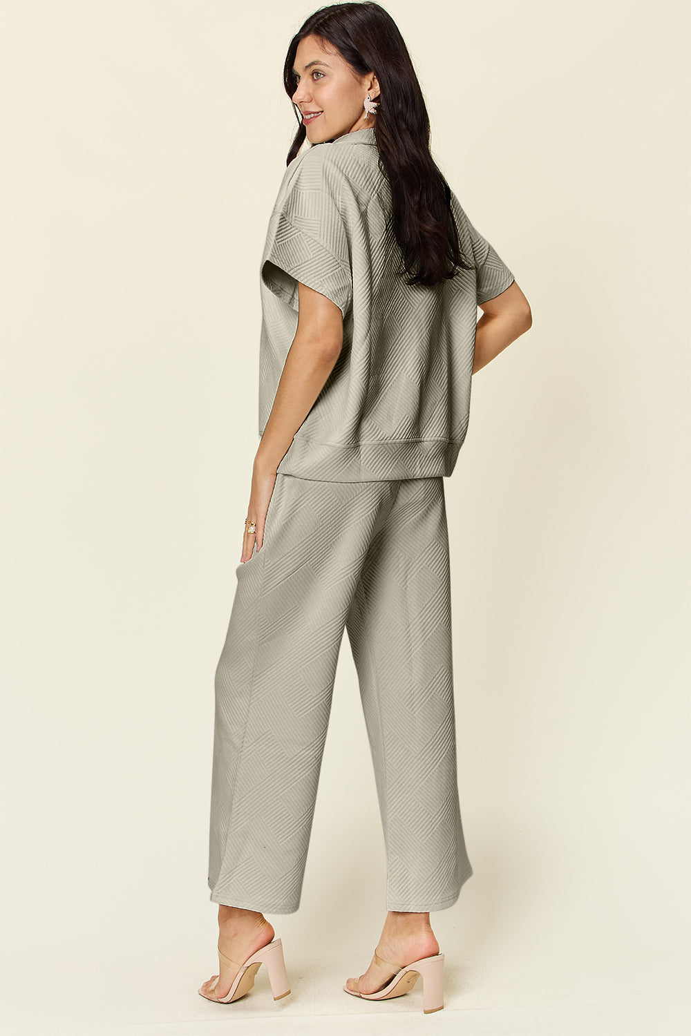 Woman wearing texture half zip short sleeve top and pants set with pockets, slightly stretchy material, beige color, back view.