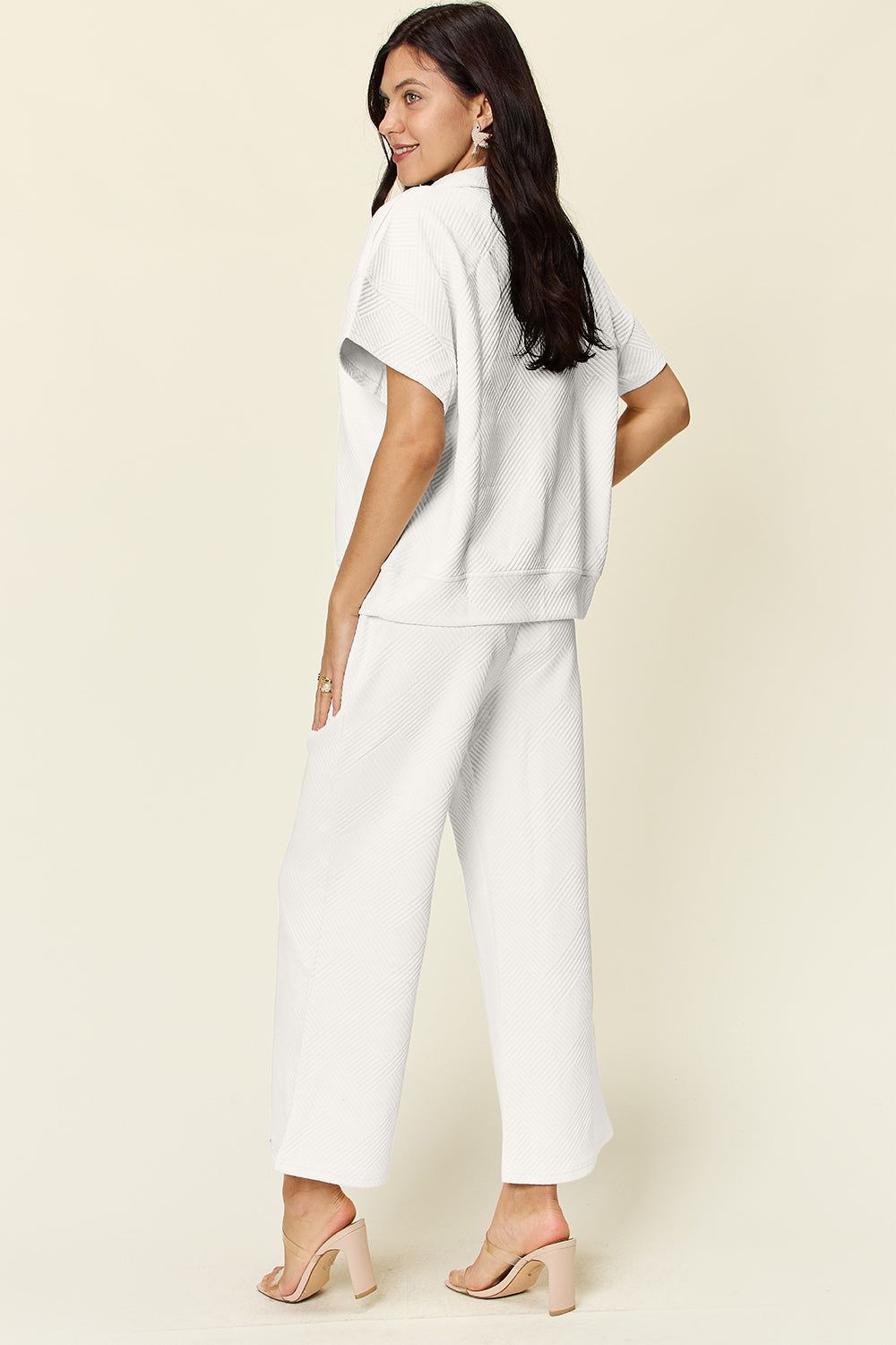 Woman wearing a white texture half zip short sleeve top and pants set with pockets and drawstring, slightly stretchy fabric.