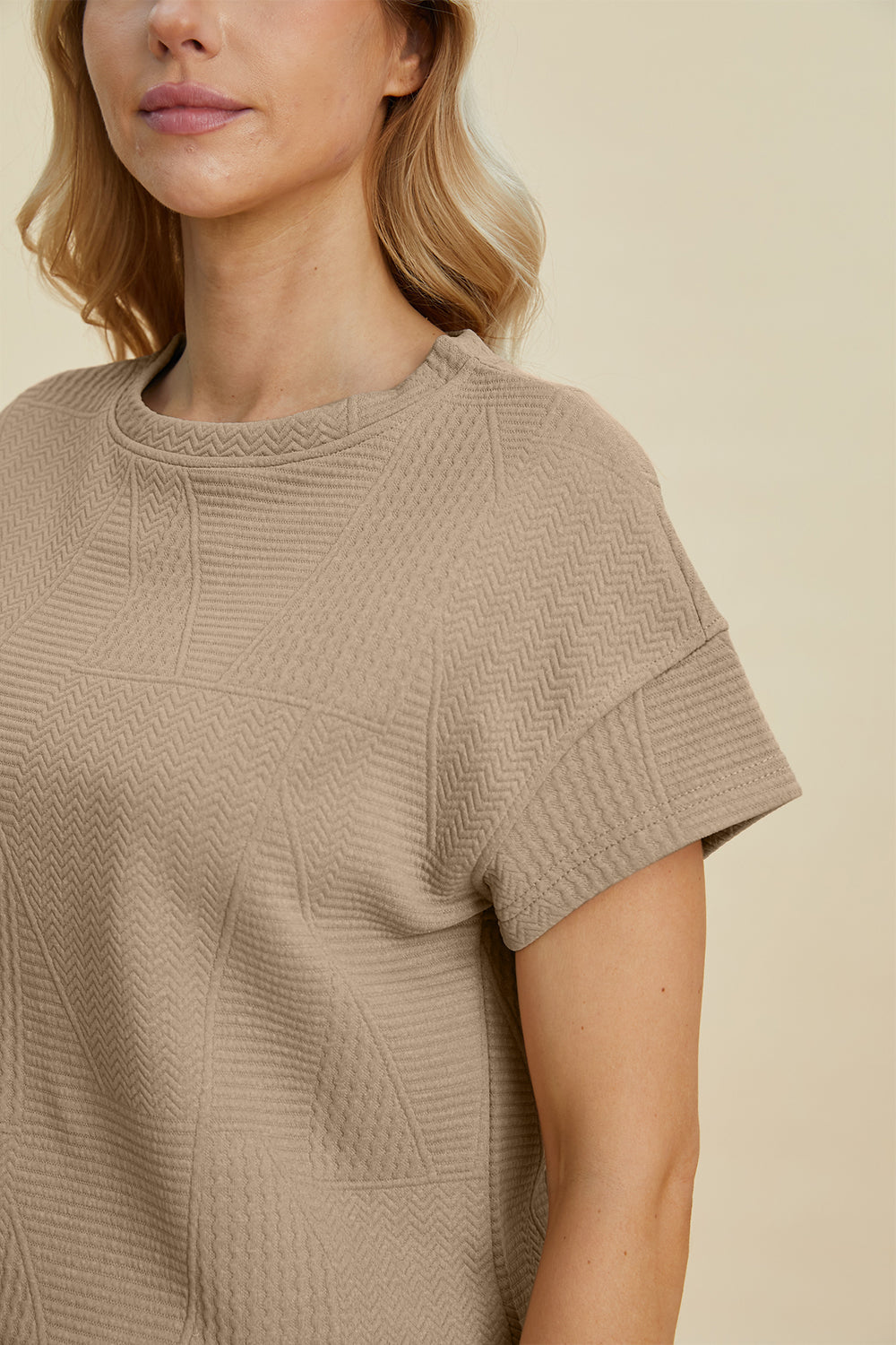 Woman wearing a beige textured short sleeve top with zigzag patterns.