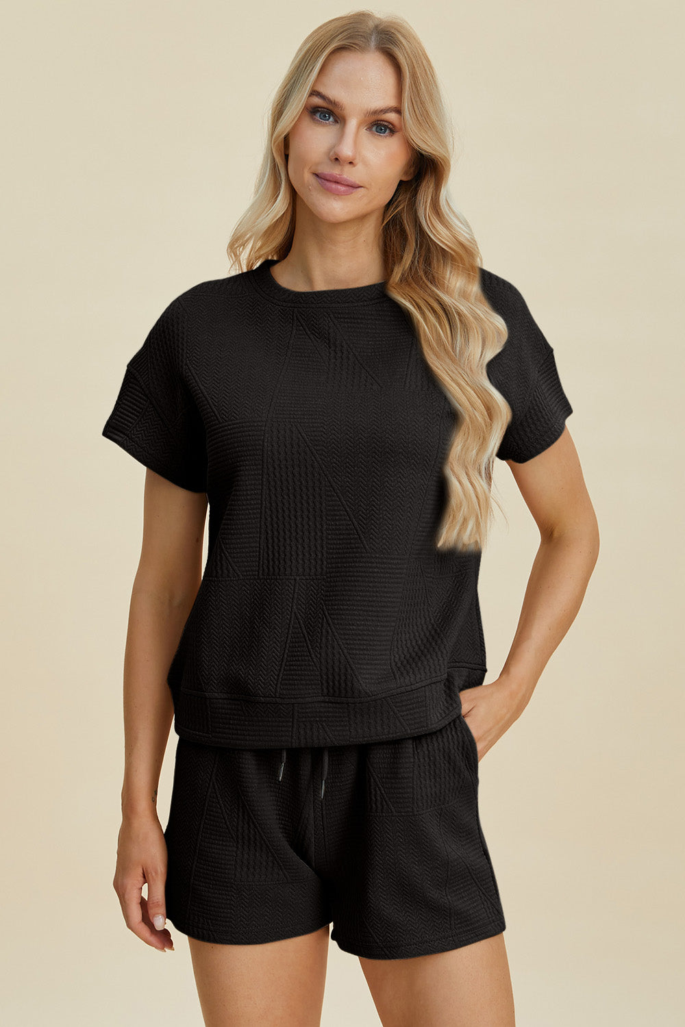 Woman wearing a full size textured short sleeve top and shorts set with pockets and drawstring, in black, made of polyester and elastane.