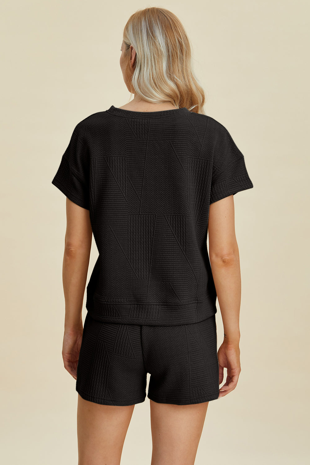 Woman wearing black full-size texture short sleeve top and shorts set, featuring pockets and drawstring, made from polyester and elastane.