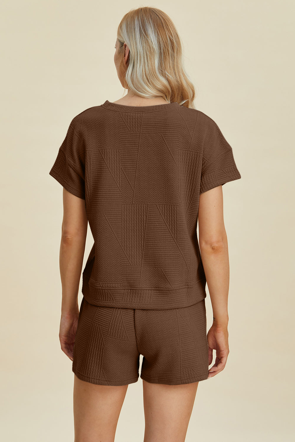 Woman wearing a brown full-size textured short sleeve top and shorts set, featuring pockets and a drawstring, made of polyester-elastane.