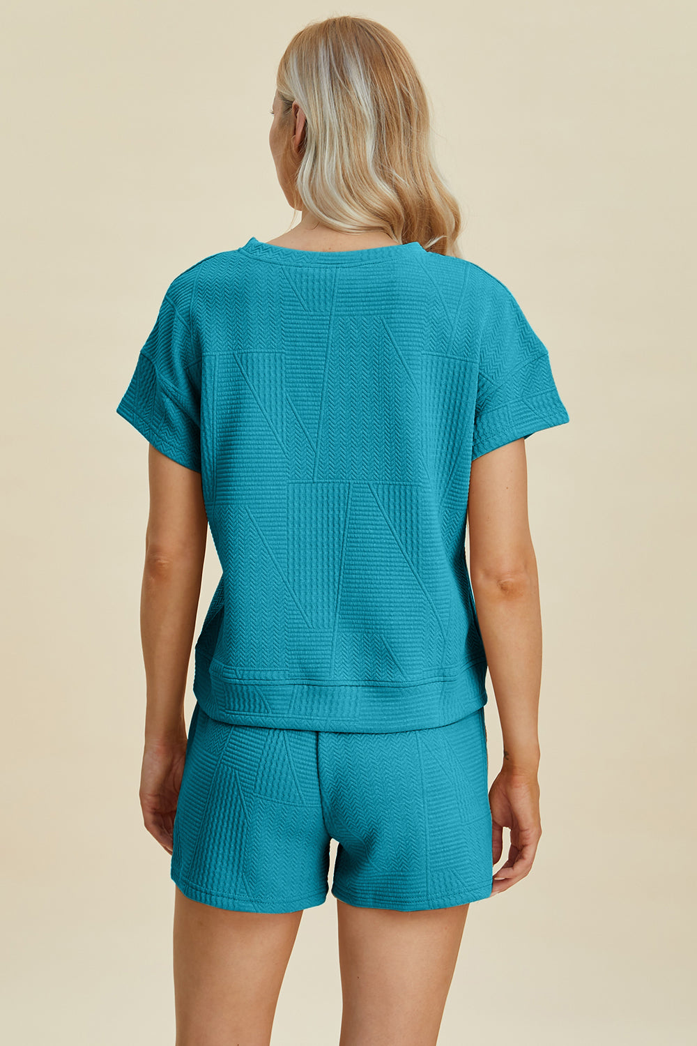 Woman in a teal full-size textured short sleeve top and shorts set, featuring pockets and a drawstring, made of polyester and elastane.