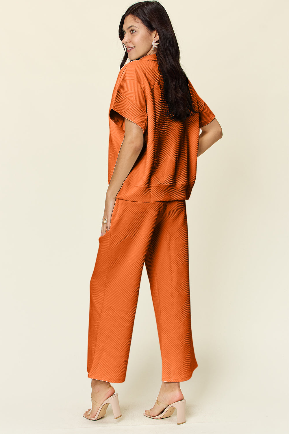 Woman wearing orange full size texture half zip short sleeve top and pants set, featuring pockets and drawstring, slightly stretchy.