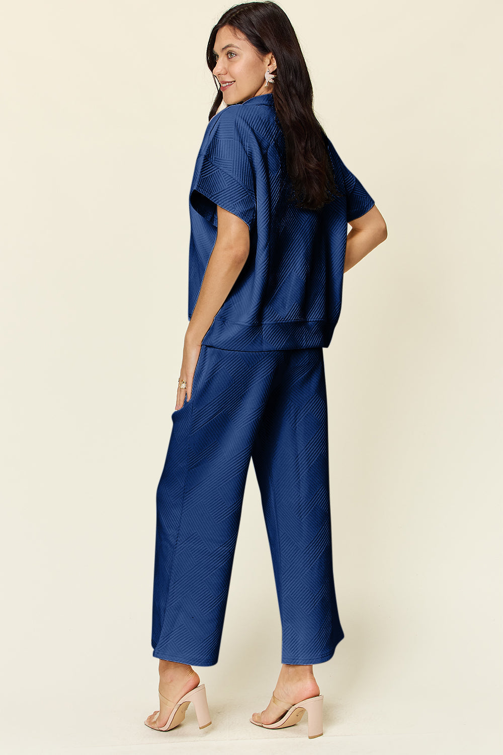 Woman wearing full size texture half zip short sleeve top and pants set in blue with pockets and drawstring, side view.