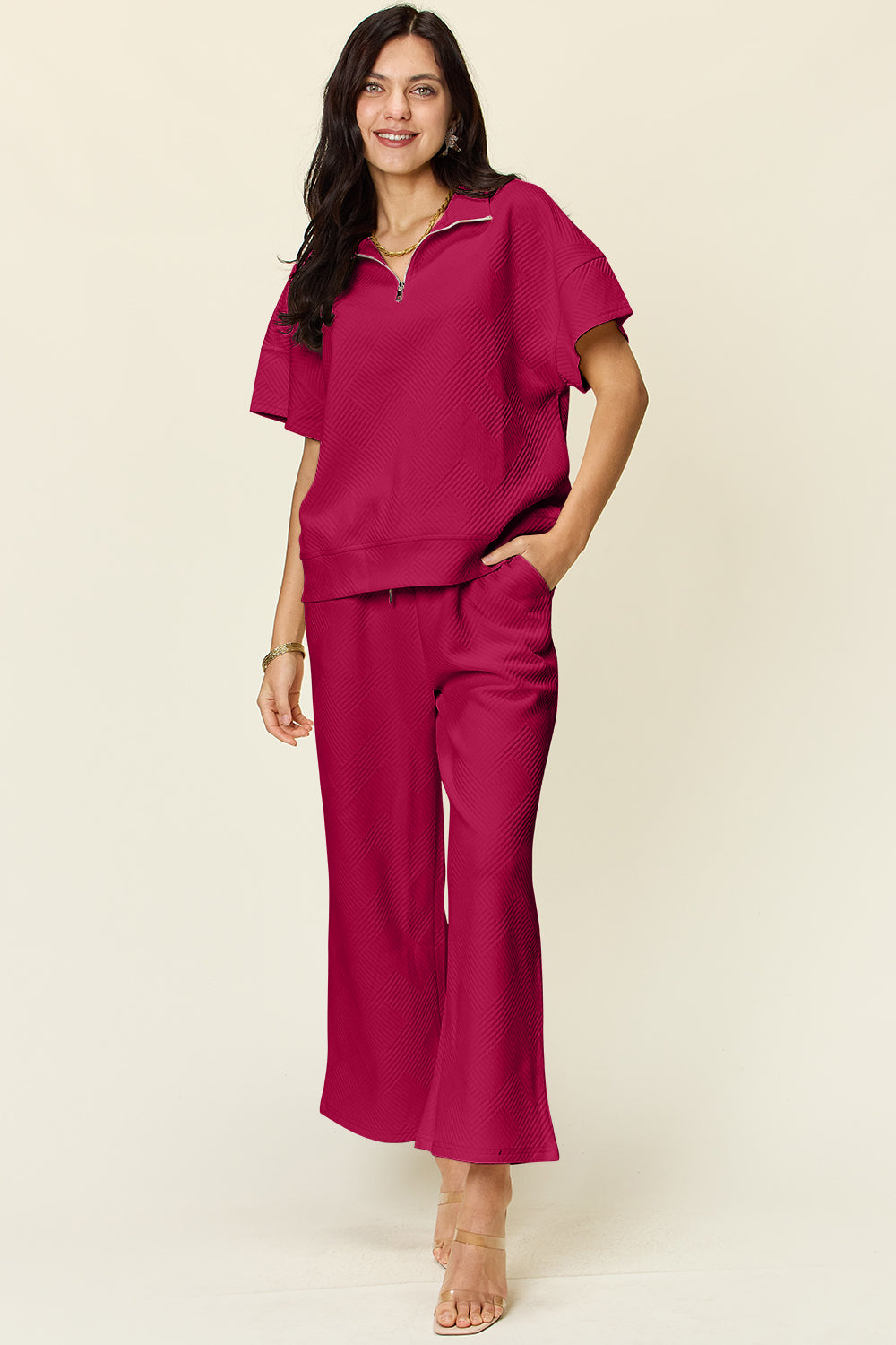 Woman wearing pink full-size half zip short sleeve top and pants set with pockets and drawstring, made of slightly stretchy polyester blend.