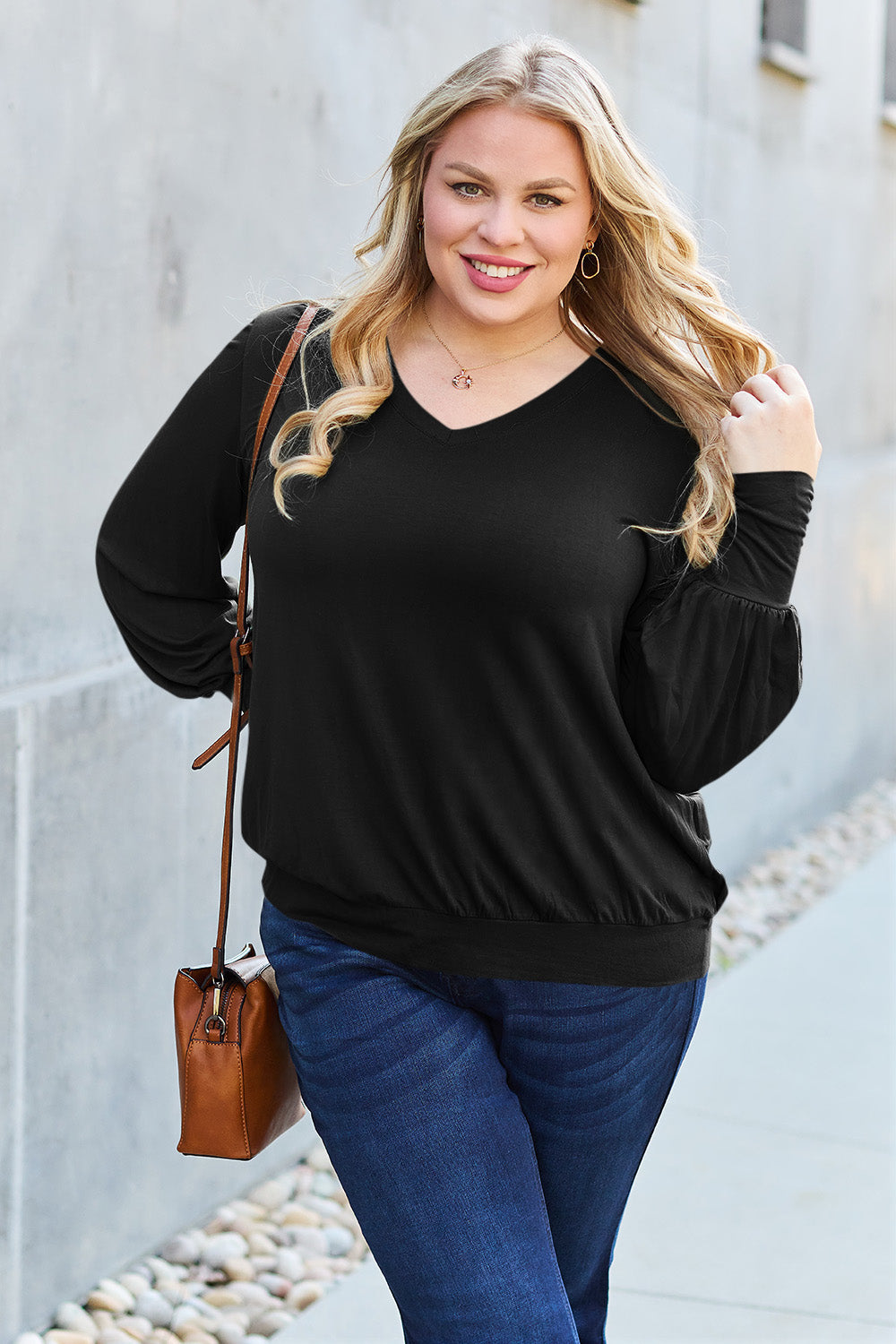 Woman wearing black V-neck lantern sleeve top with jeans, accessorized with a brown shoulder bag, walking outdoors.