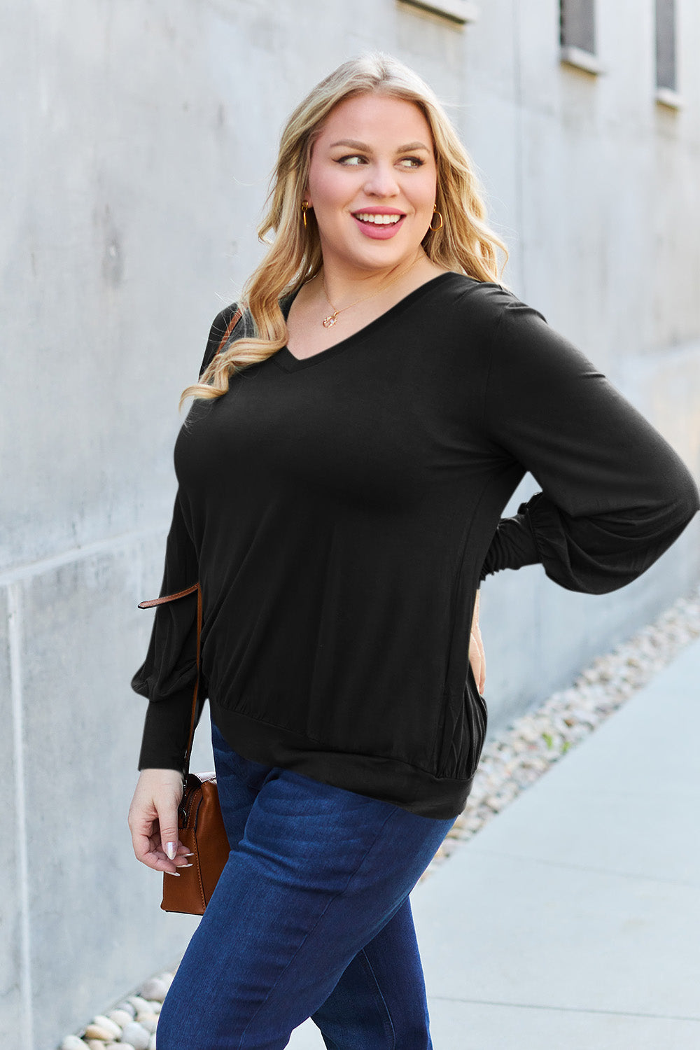 Woman wearing a black V-neck lantern sleeve top made of rayon and spandex, styled casually with jeans, standing on a sidewalk.