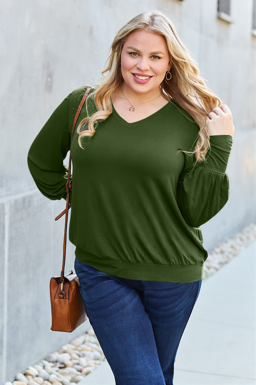 Woman wearing a stylish green V-neck lantern sleeve top, perfect for casual outings, paired with blue jeans and a brown shoulder bag.