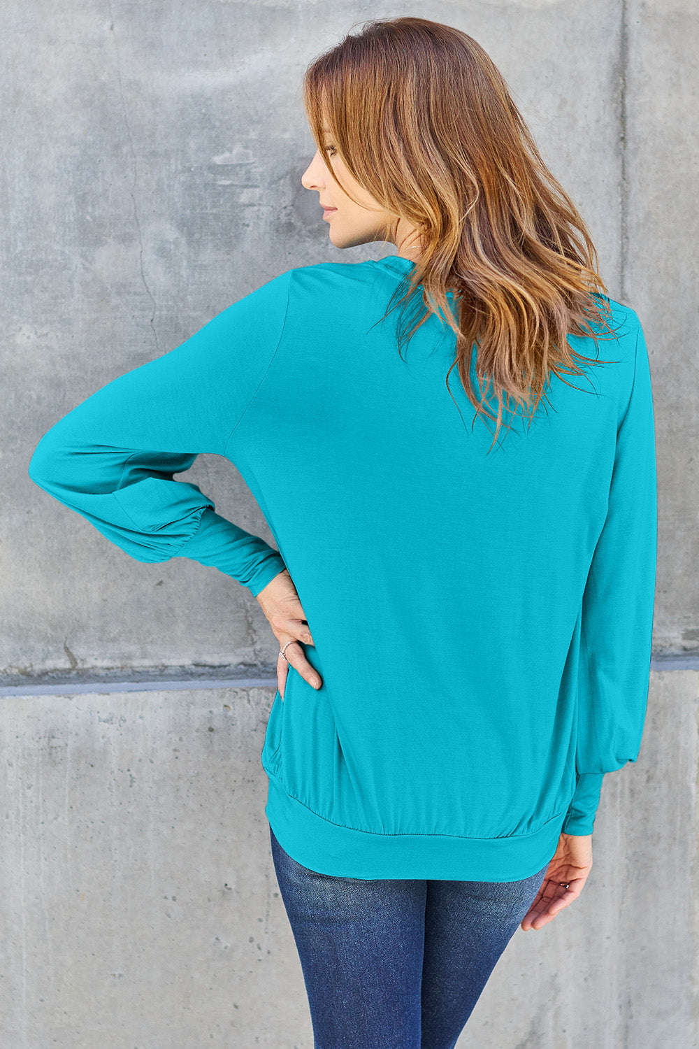 Woman wearing a teal V-neck lantern sleeve top with a slightly stretchy fit, made from 95% rayon and 5% spandex.