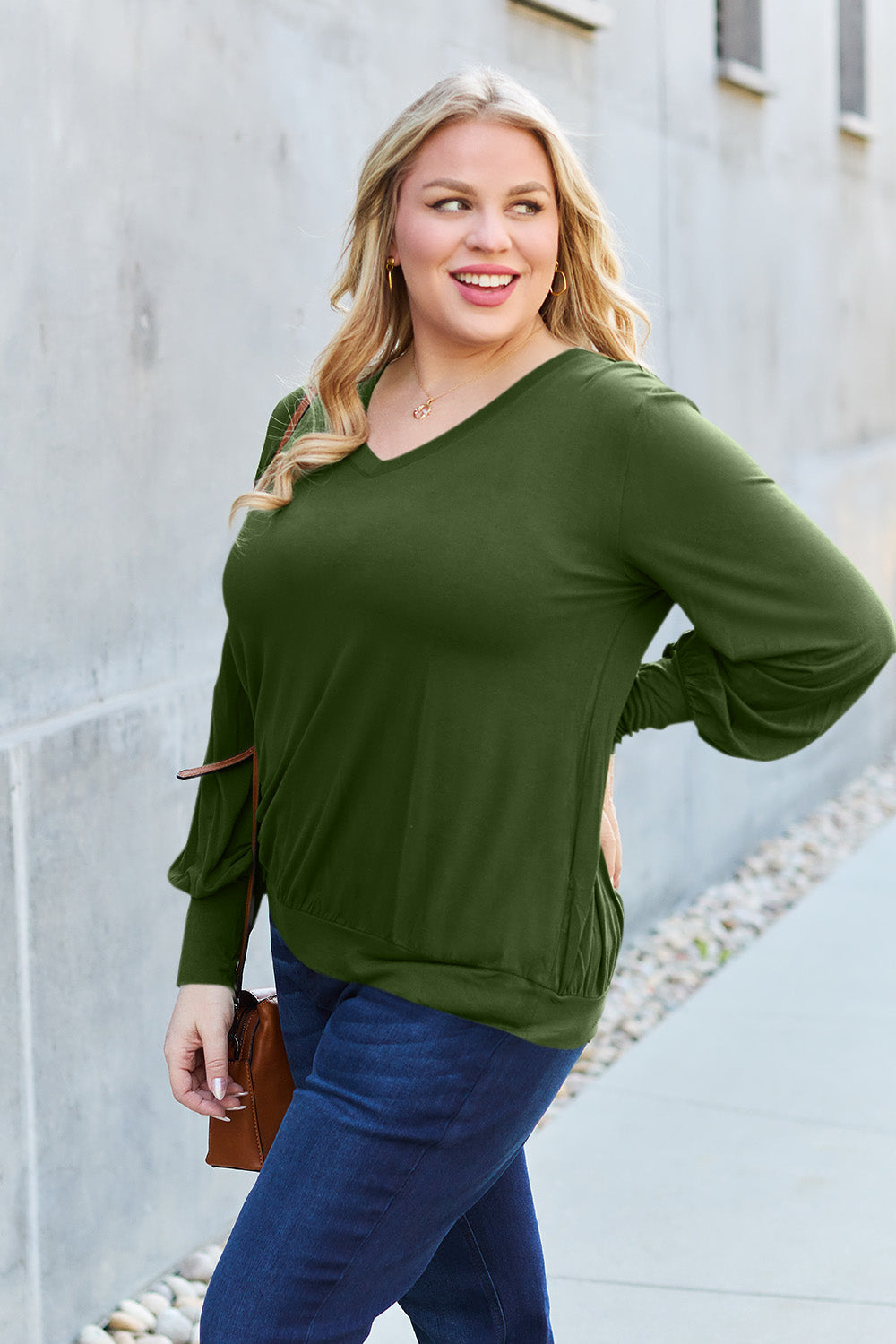 Woman wearing green V-neck lantern sleeve top made of 95% rayon and 5% spandex, standing outdoors.