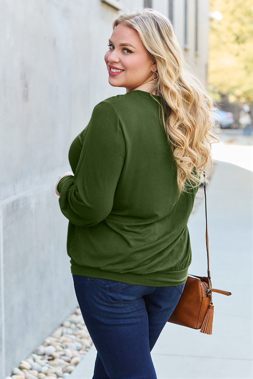 Woman in green V-neck lantern sleeve top with handbag, smiling while walking outside.