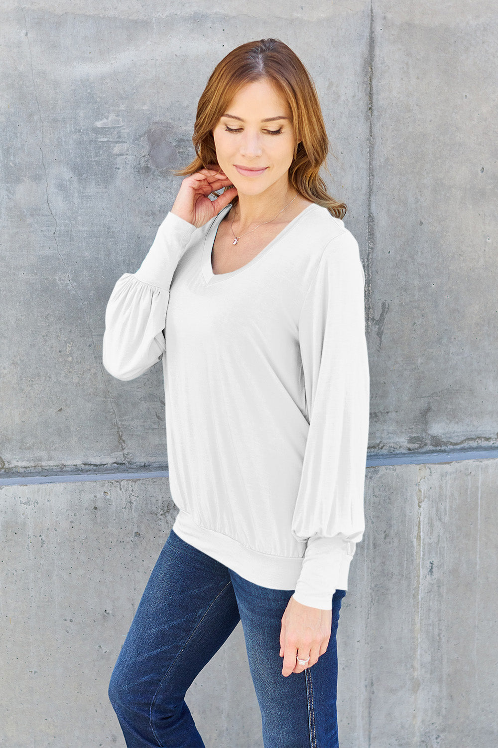 Woman wearing a white V-neck lantern sleeve top with jeans, showcasing a casual and stylish look.