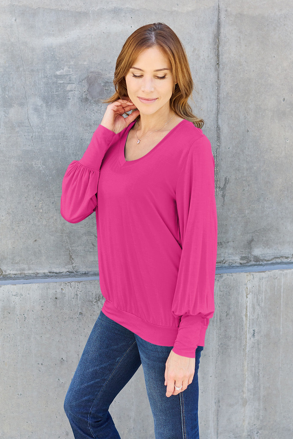 Woman wearing a pink V-neck lantern sleeve top with jeans, showcasing a stylish and casual outfit.