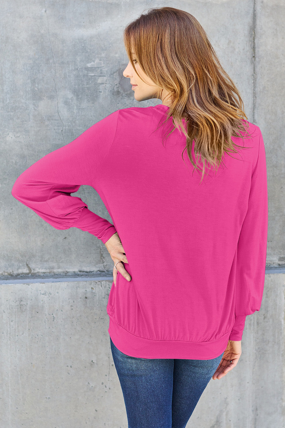 Woman wearing pink V-Neck Lantern Sleeve Top with slightly stretchy, opaque fabric, standing against a concrete wall.