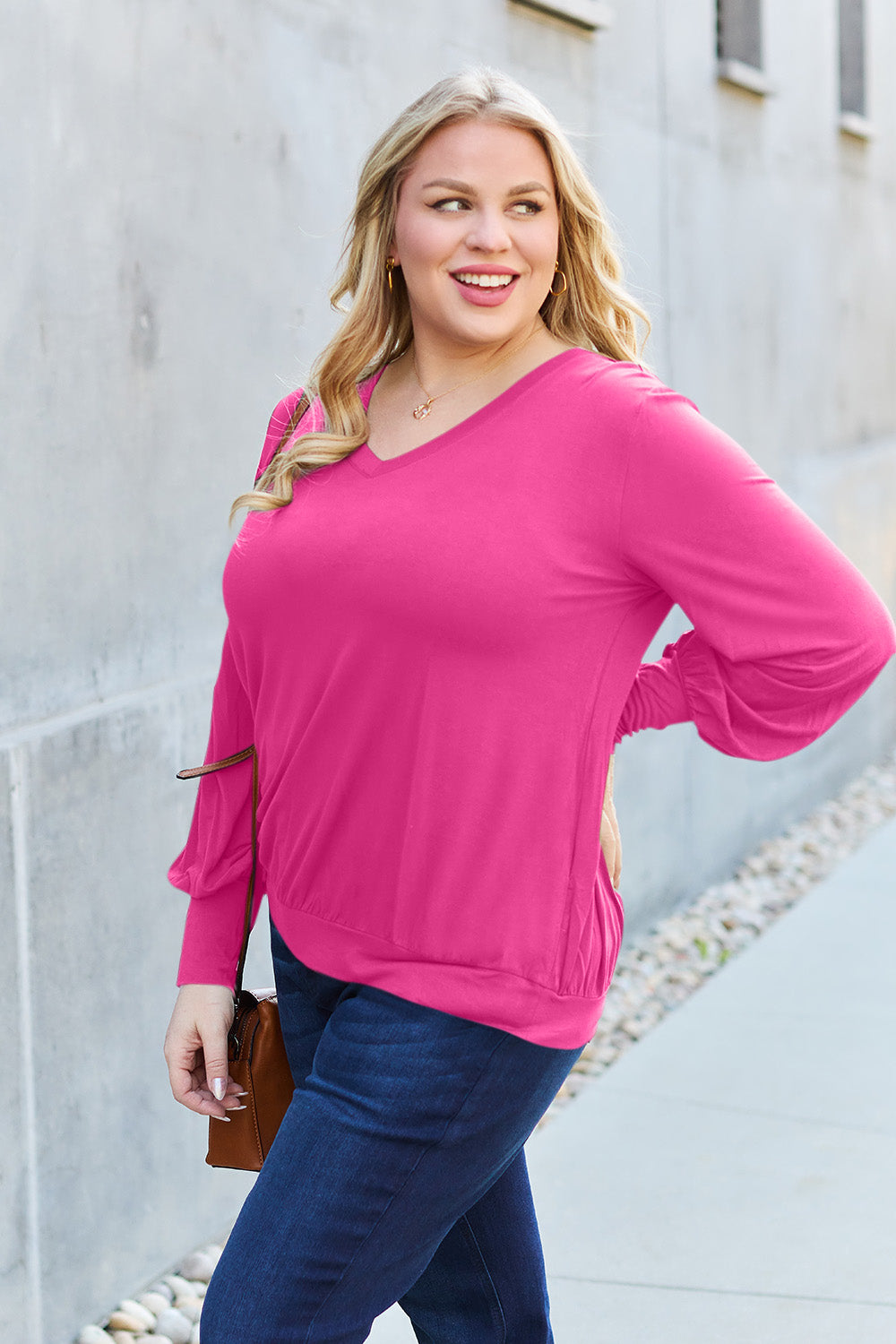 Woman wearing a pink V-neck lantern sleeve top made of rayon and spandex, styled with dark jeans and a casual purse.