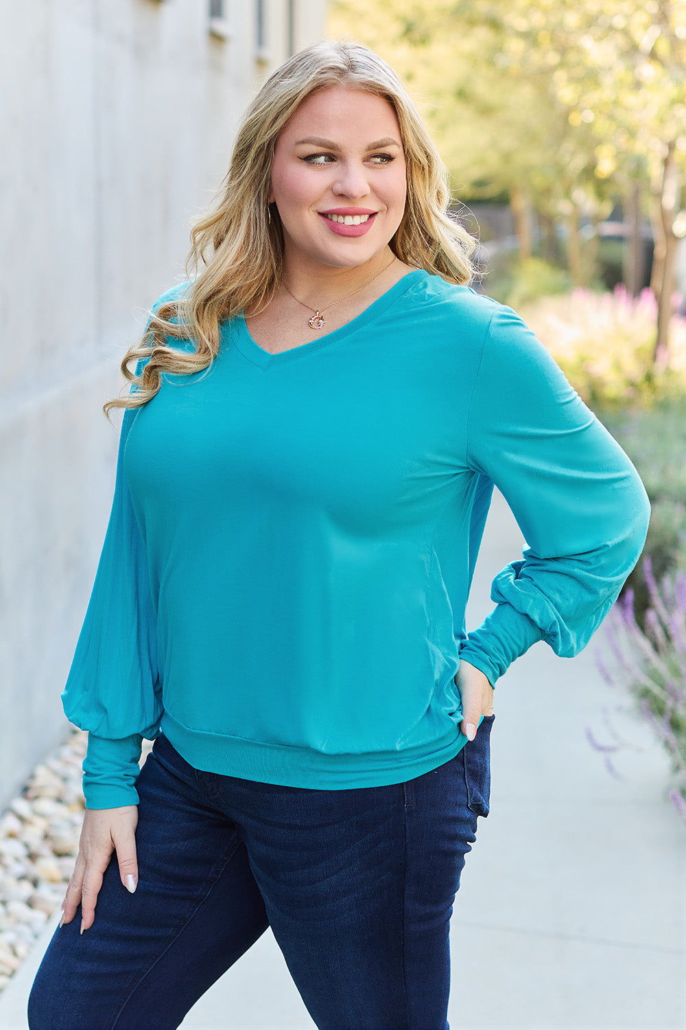 Woman wearing a teal V-neck lantern sleeve top with slightly stretchy fit, made from 95% rayon and 5% spandex.