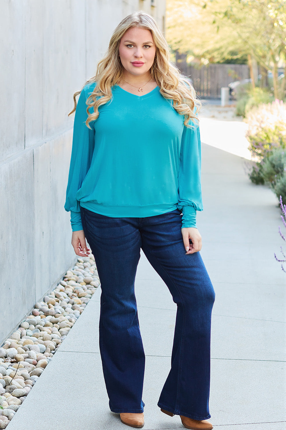 Woman wearing a V-neck lantern sleeve top in teal with dark jeans, outdoor setting.