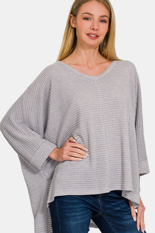 Woman wearing a gray waffle knit V-neck long sleeve slit top with high-low hemline, paired with jeans.