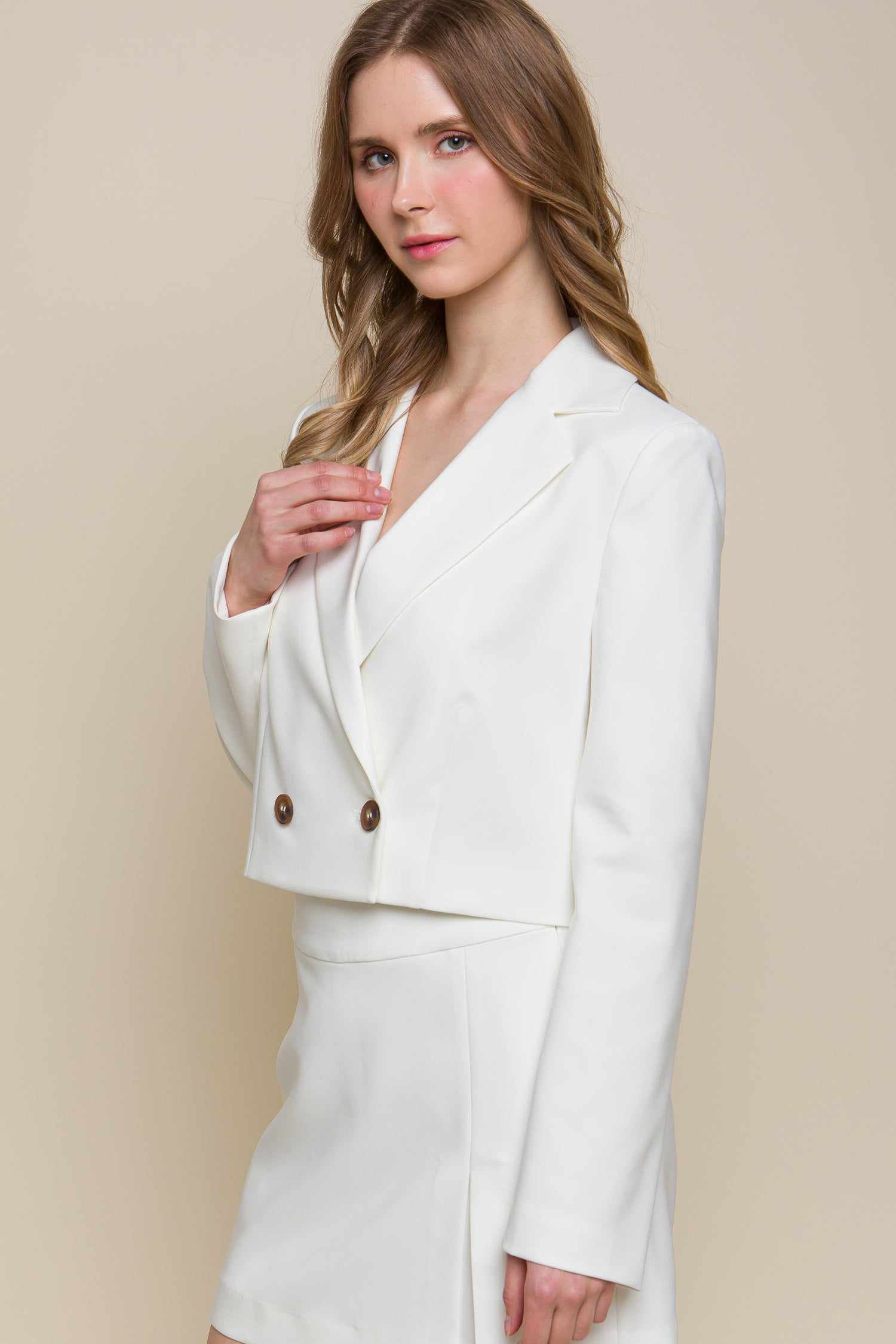 Woman wearing a white button crop blazer, made from 95% polyester and 5% spandex, featuring a chic and modern design.