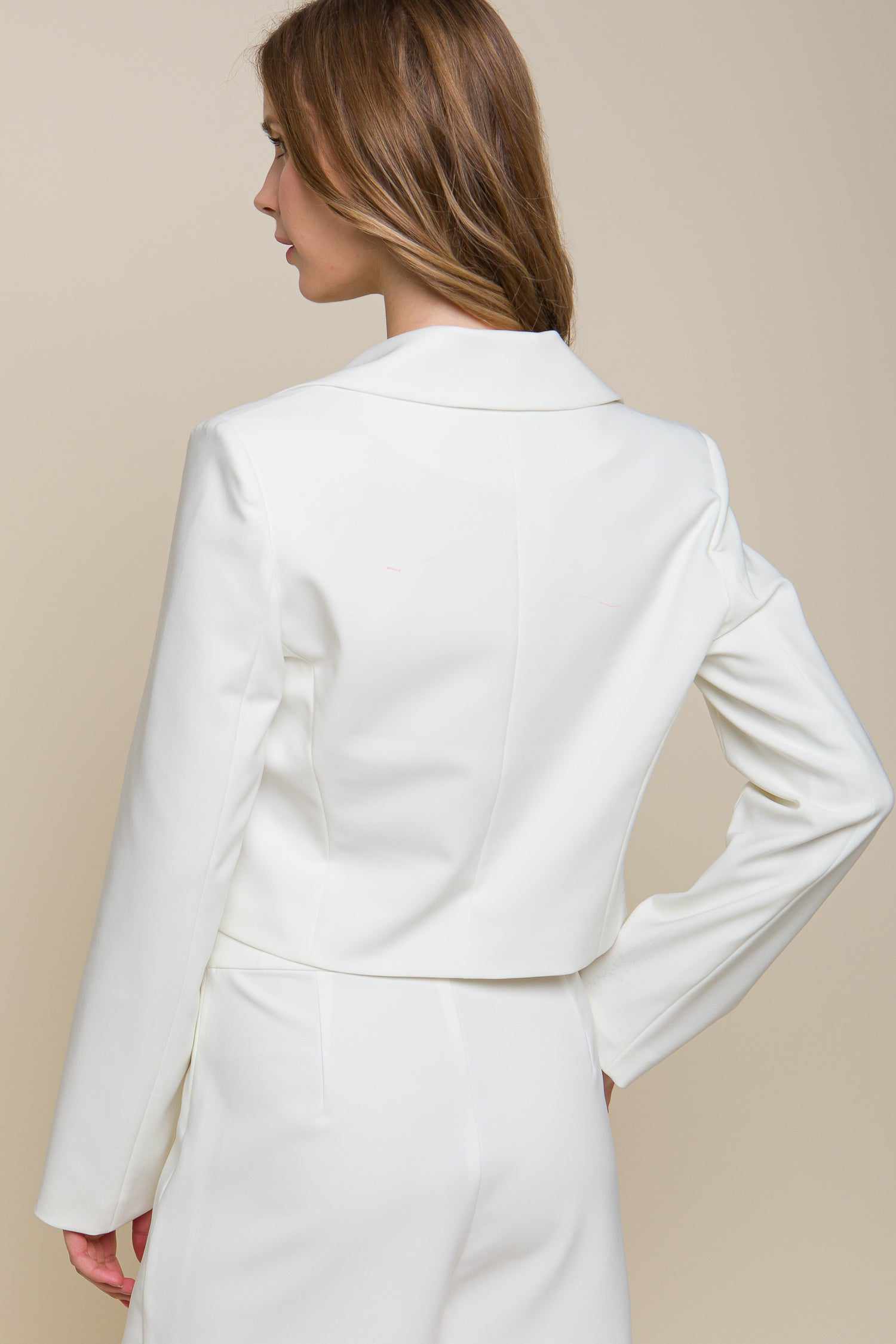 Woman wearing a white button crop blazer made of polyester and spandex, viewed from the back.