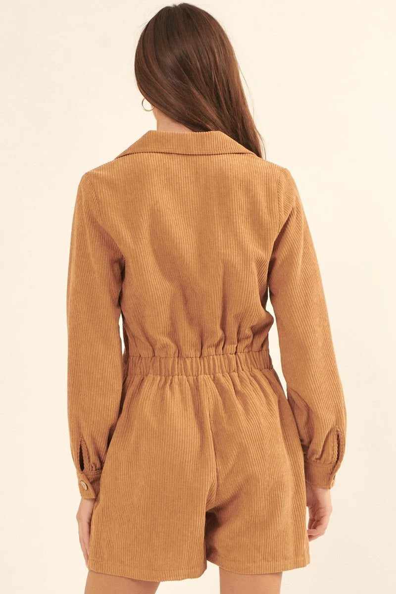 Woman wearing taupe woven corduroy romper with lapel collar, elastic waist, long sleeves, and wide legs seen from the back.