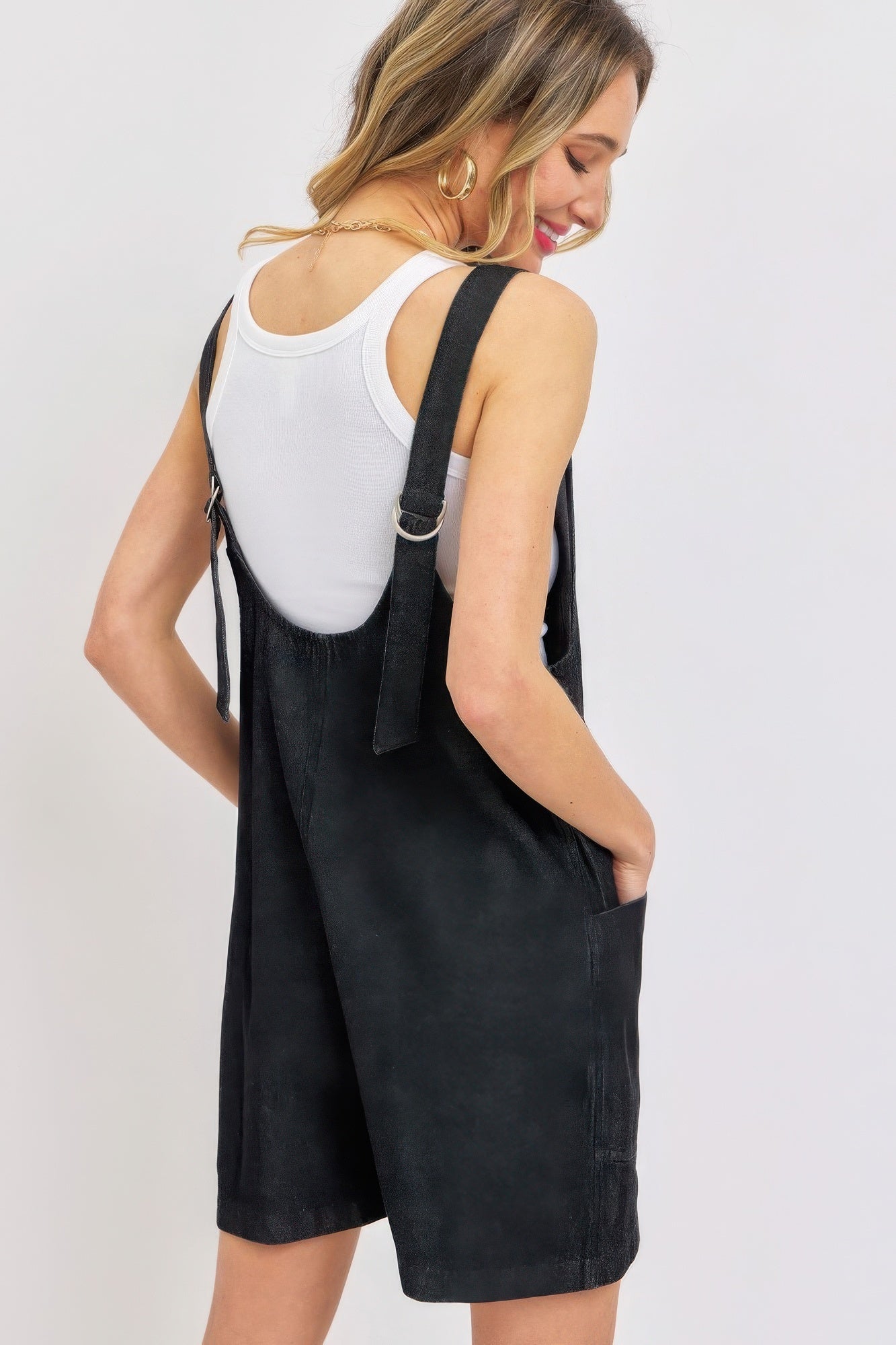 Woman wearing a black summer denim overall romper with adjustable straps and oversized pockets, showcasing a casual summer look.