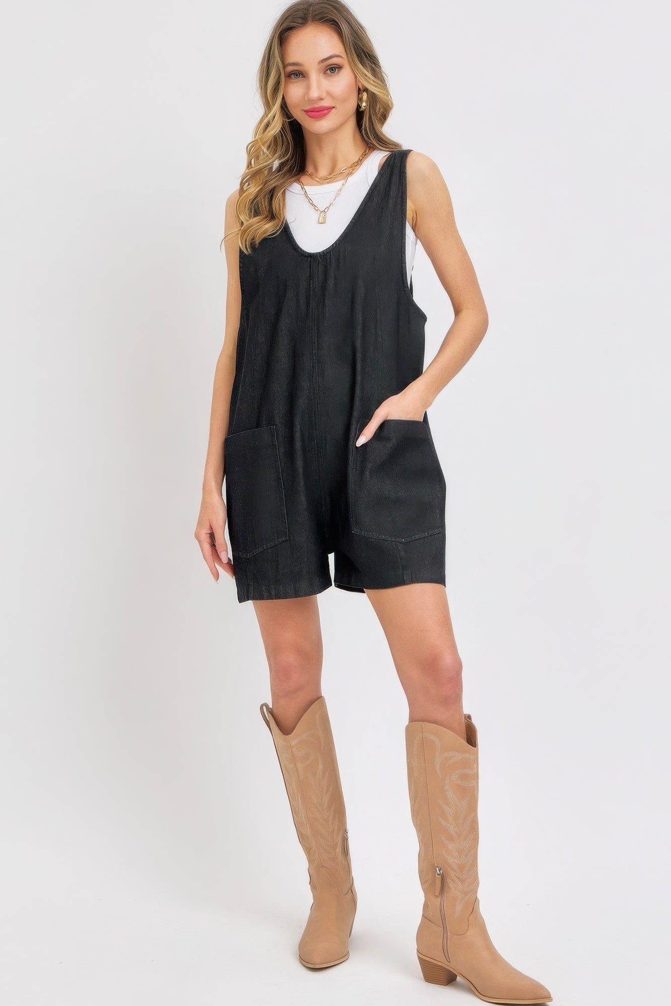 Woman in stylish summer denim overall romper with oversized pockets and adjustable straps, accessorized with boots.