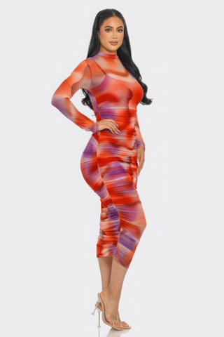 Woman wearing vibrant tomato and purple print mesh ruched midi dress with long sleeves and sophisticated smock neck.