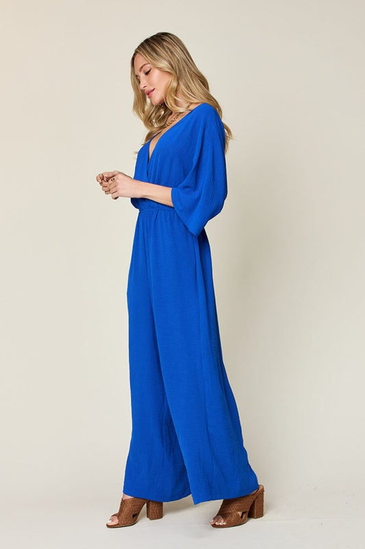 Woman wearing blue surplice wide leg jumpsuit with pockets, featuring tied and ruched details, made of polyester and spandex.