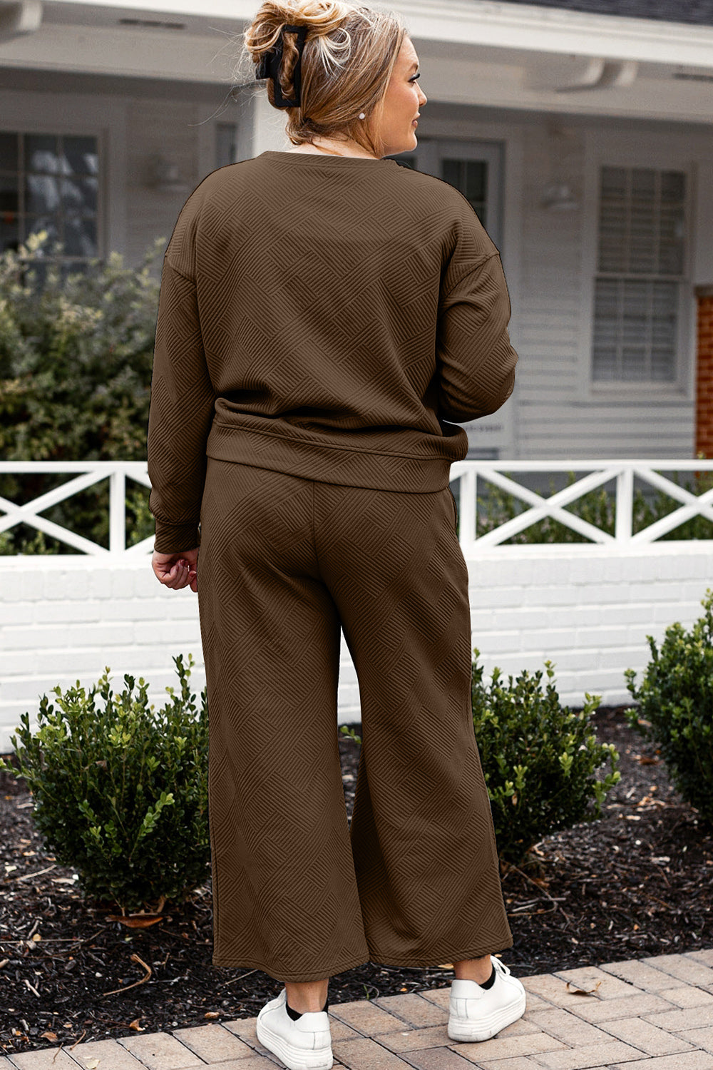 Woman wearing textured long sleeve top and drawstring pants set, slightly stretchy, standing in garden setting.