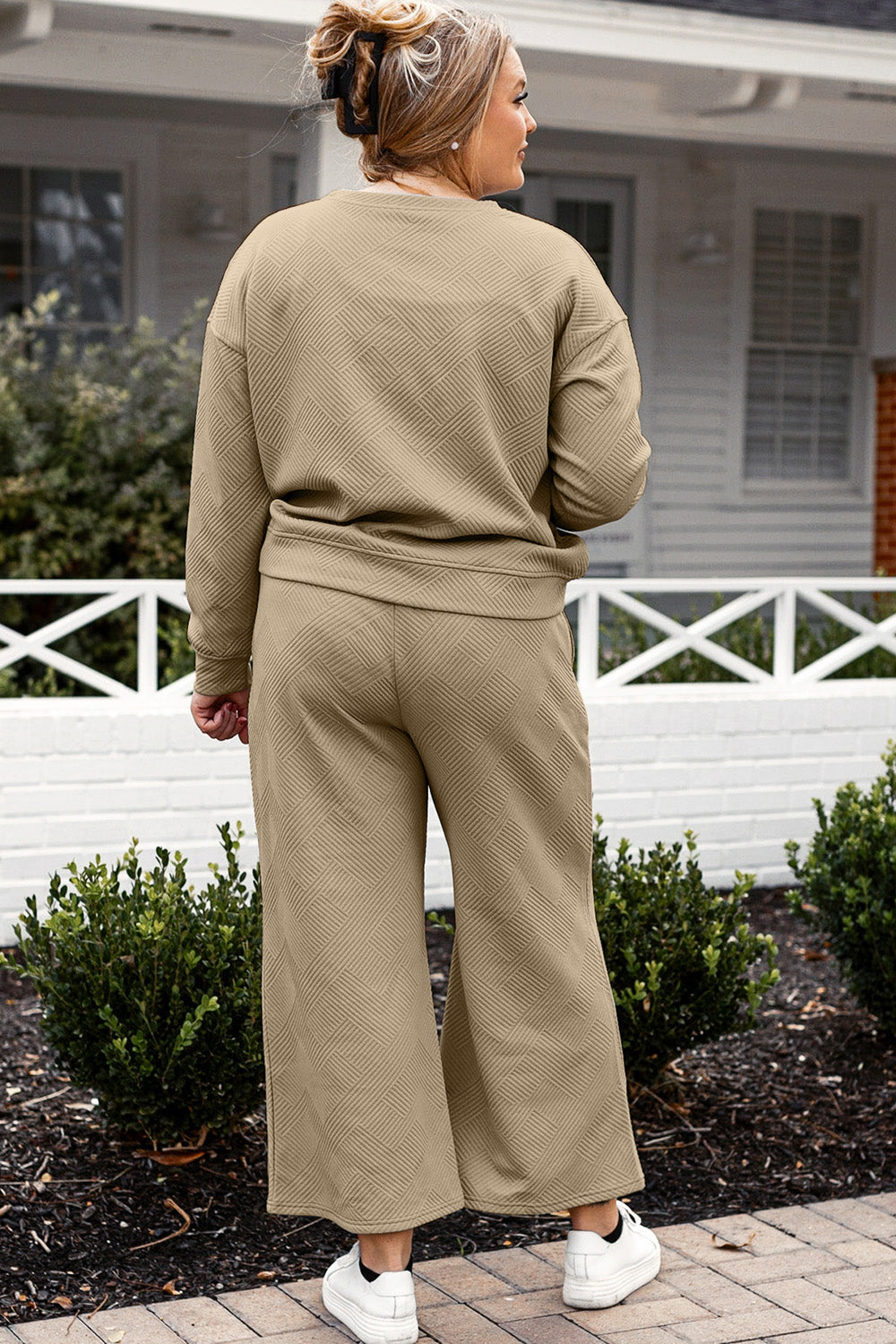 Woman wearing a textured long sleeve top and drawstring pants set in olive green, standing outdoors near a white house and green bushes.