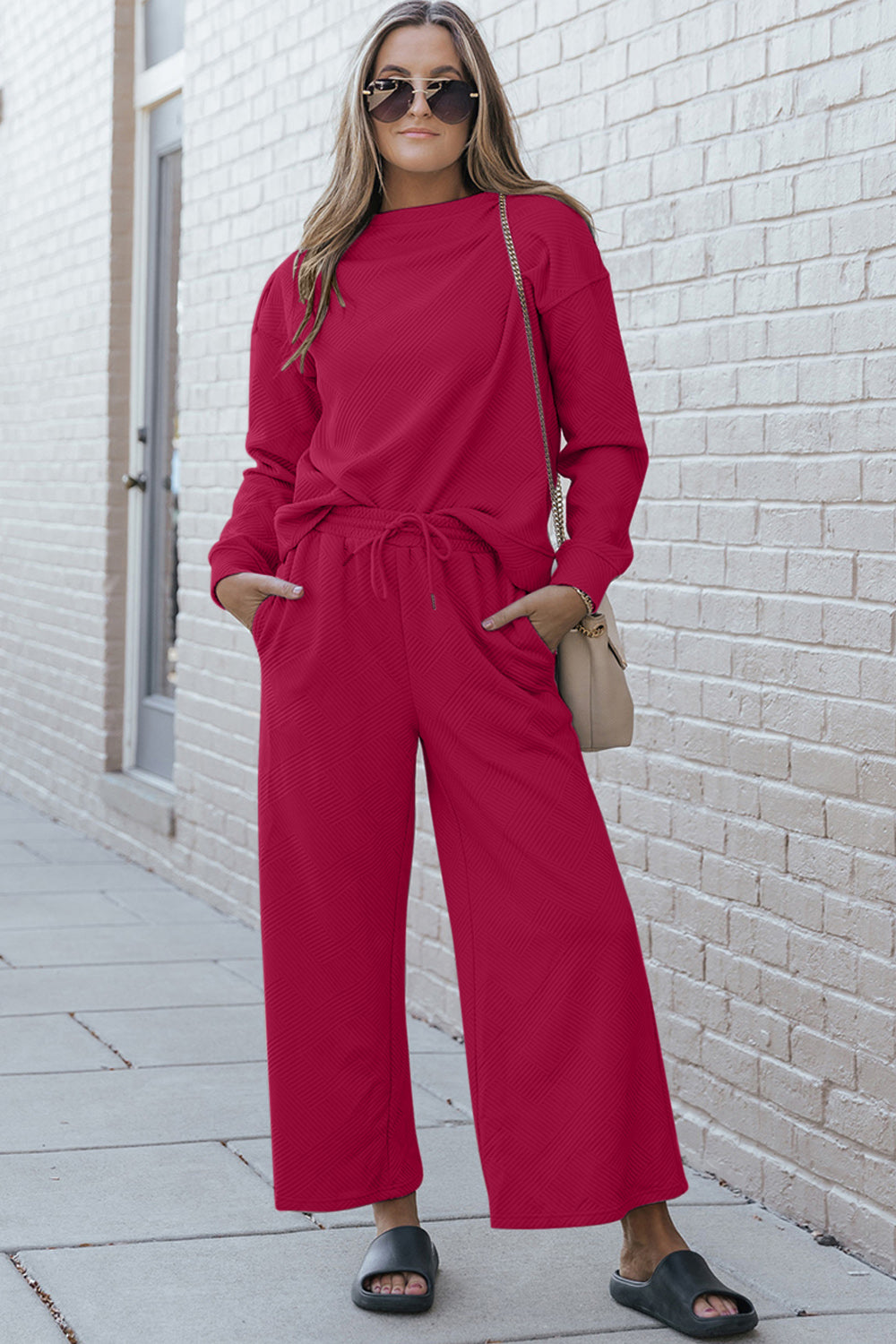 Stylish model wearing red textured long sleeve top and drawstring pants set, complemented with sandals and sunglasses.