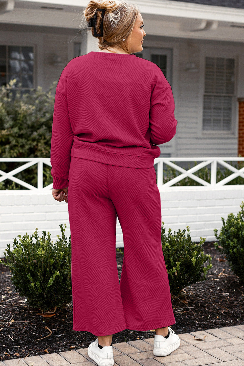 Woman in red textured long sleeve top and drawstring pants set, outdoors, showcasing slightly stretchy fabric from behind.