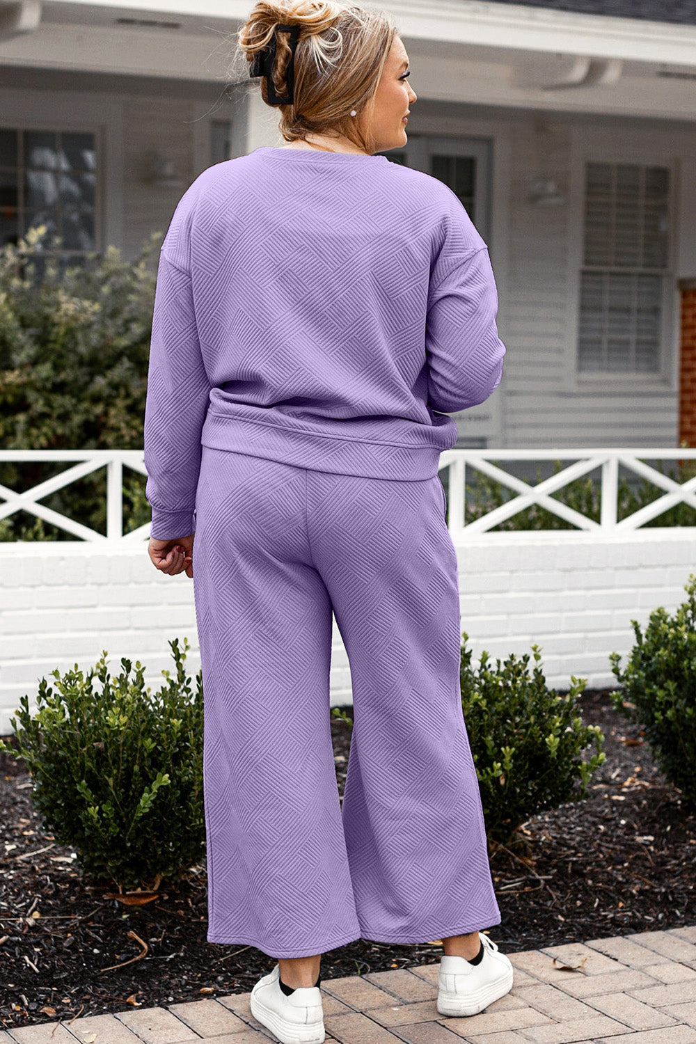 Woman wearing a lavender textured long sleeve top and drawstring pants set, standing outdoors near a white fence.