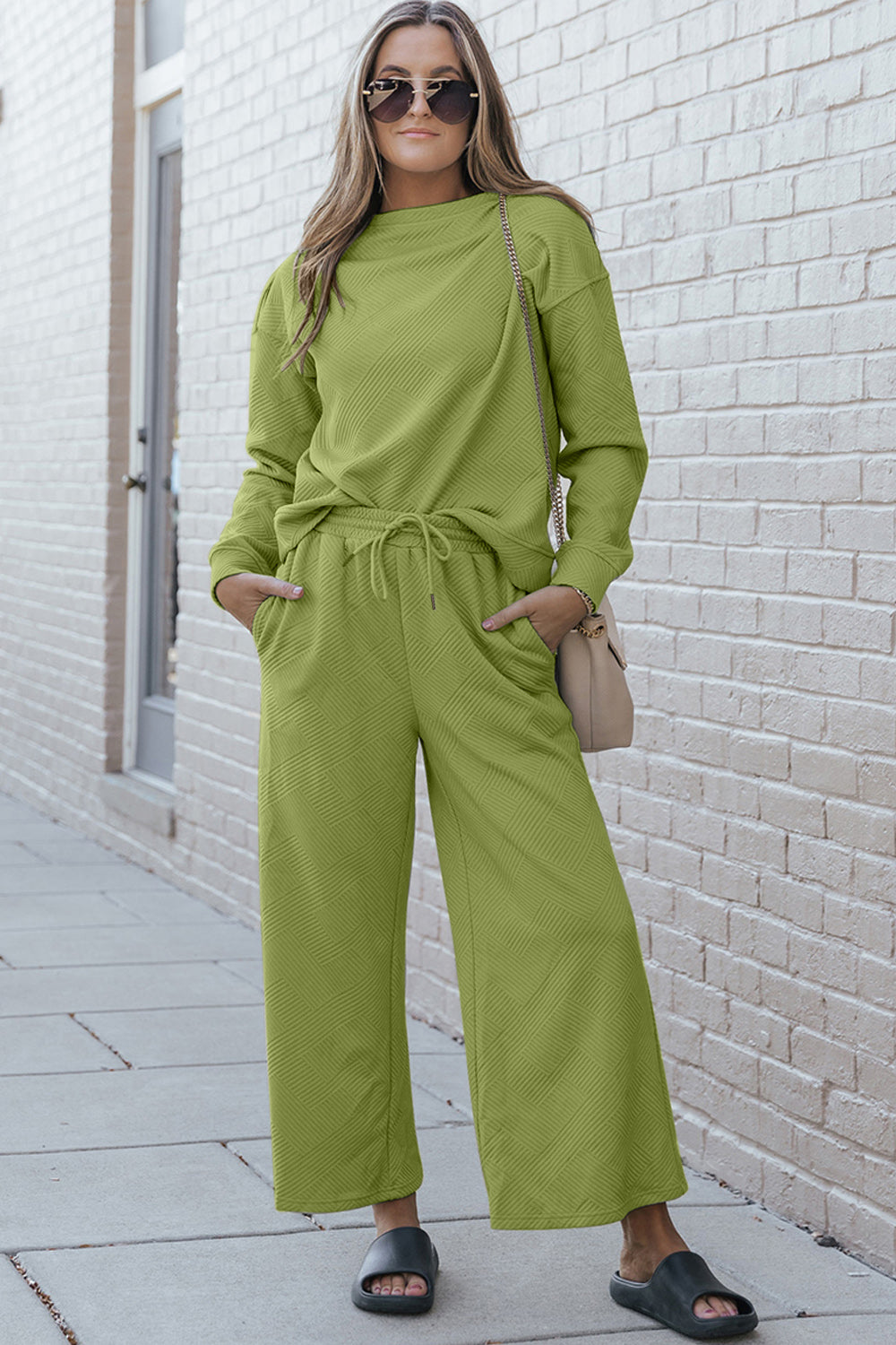 Woman wearing a textured long sleeve top and drawstring pants set in green, accessorized with sunglasses and slides.