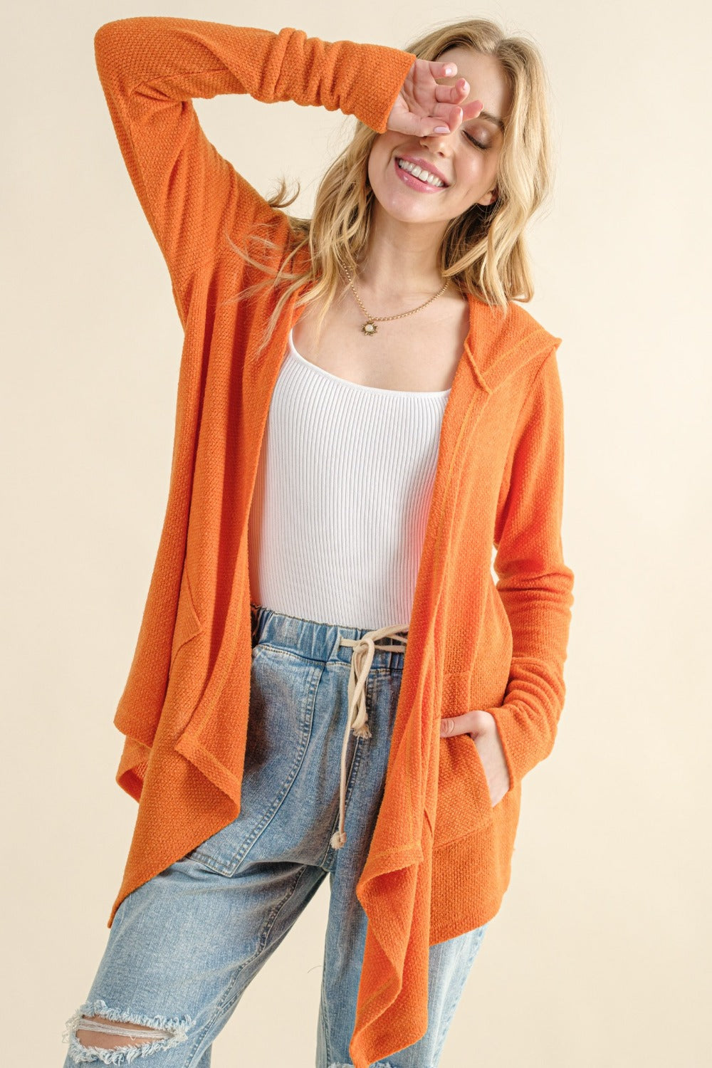 Woman wearing orange thermal hooded open front cardigan with pockets over white top and jeans