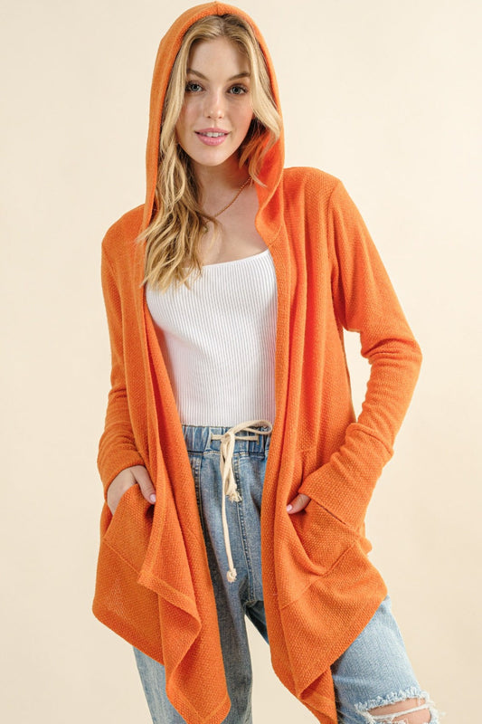 Woman wearing thermal hooded open front cardigan with pockets in orange color, showcasing casual style with blue jeans.