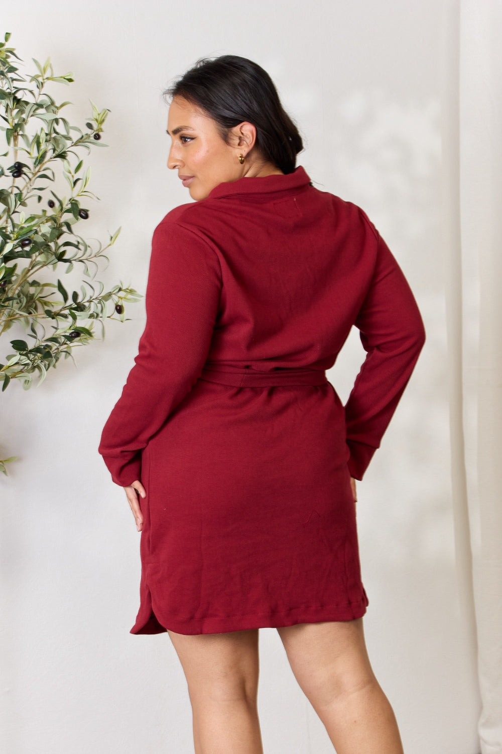 Woman wearing a red tie front half zip long sleeve shirt dress, showcasing the back style and fit in a comfortable indoor setting.