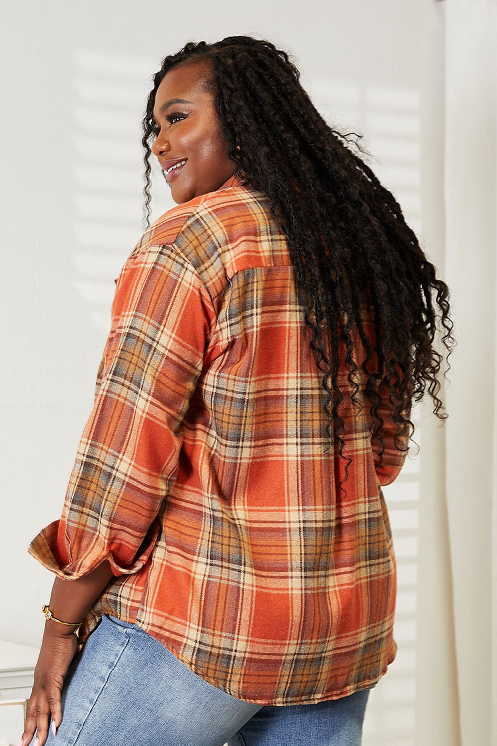 Woman wearing an orange plaid dropped shoulder shirt paired with jeans, showcasing back view and casual style.