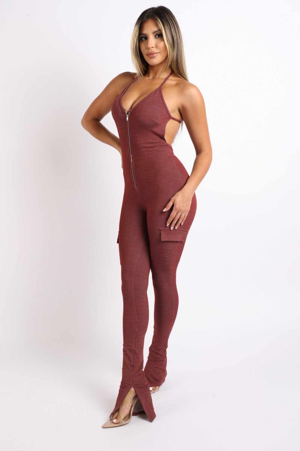 Woman wearing a brick red cargo pocket halter jumpsuit made of rayon, polyester, and spandex, showing side pockets and zipper front design.