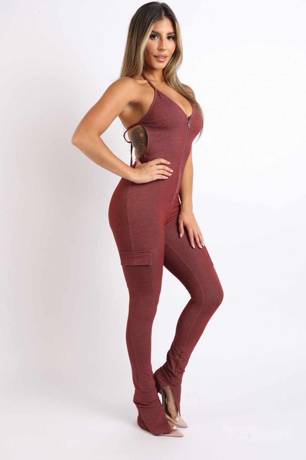 Woman wearing a brick-colored cargo pocket halter jumpsuit made of rayon, polyester, and spandex blend, side view.