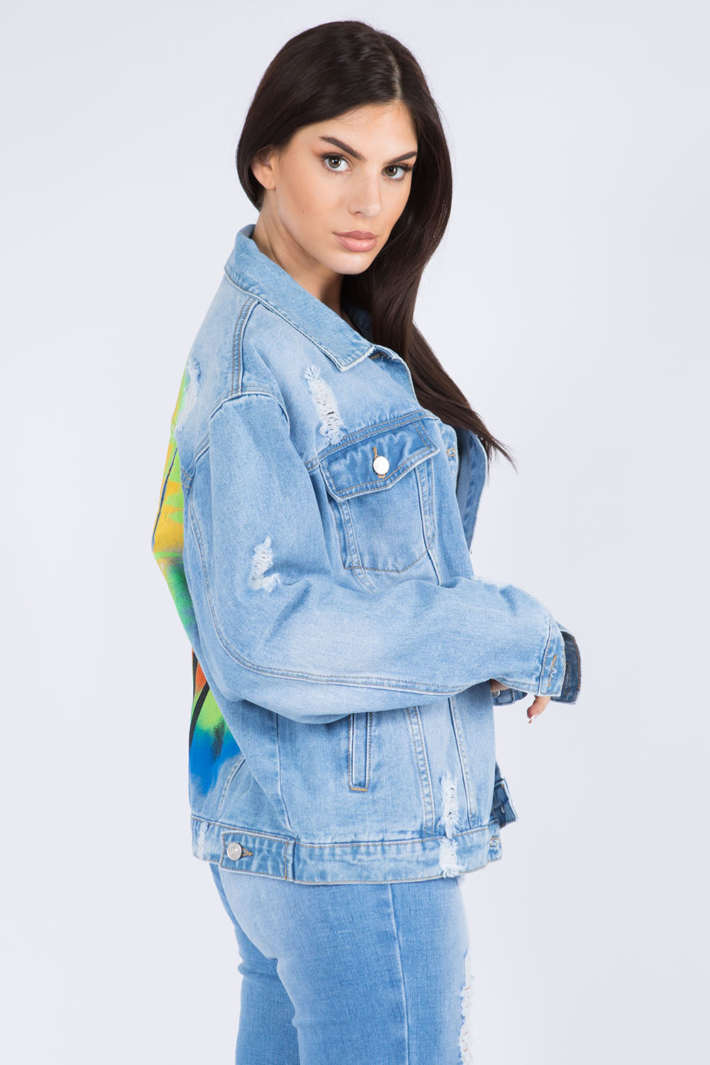 Woman wearing distressed denim jacket with artistic painted back design, showcasing trendy casual style and relaxed fit.