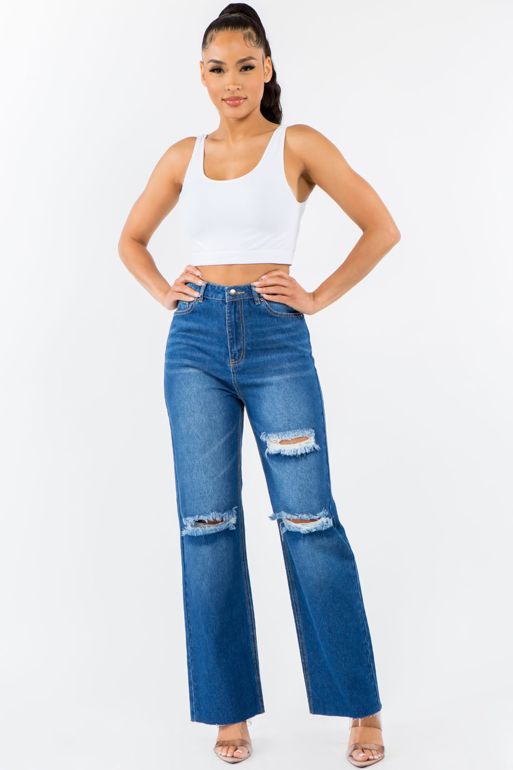 Woman wearing high waist distressed wide leg jeans with a white tank top, showcasing trendy raw hem and versatile denim wash.