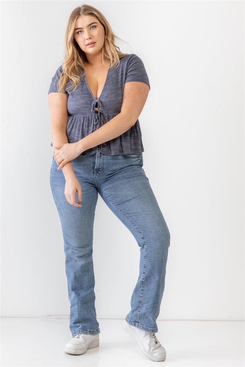 Plus size model wearing a denim blue blouse with a flare hem and tie details, paired with jeans, showcasing a stylish and trendy look.