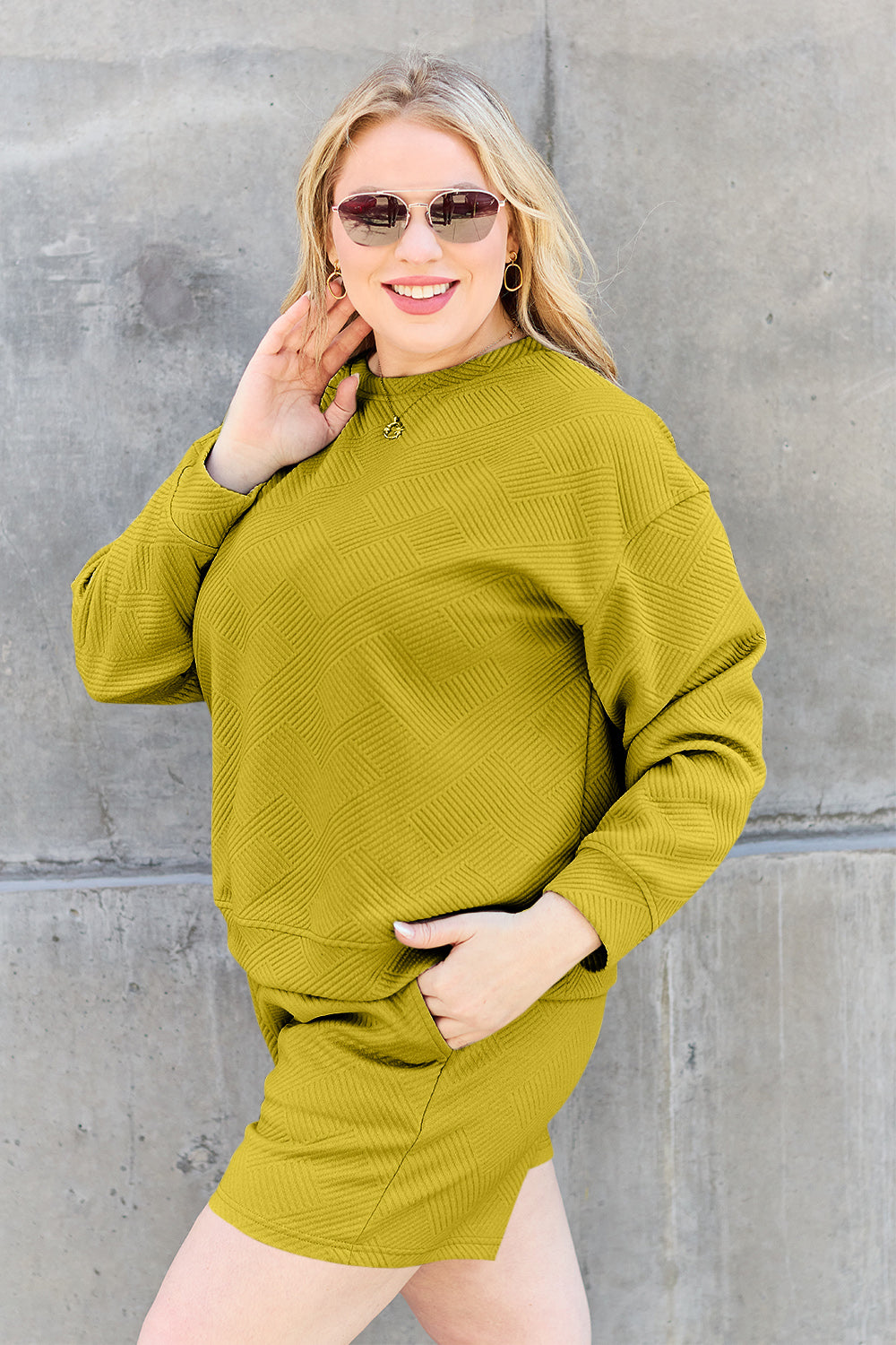 Woman wearing mustard textured long sleeve top and drawstring shorts set with pockets, posing against a concrete wall.